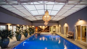 Una piscina interior con techo de vidrio, plantas en macetas y un banco.