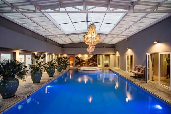 An indoor swimming pool with a glass ceiling, potted plants, and a bench. - Majeka House Boutique Hotel (Stellenbosch)