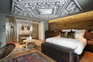 A modern bedroom with a large bed, a wooden headboard, a sofa, a coffee table, and a patterned rug. - Majeka House Boutique Hotel (Stellenbosch)