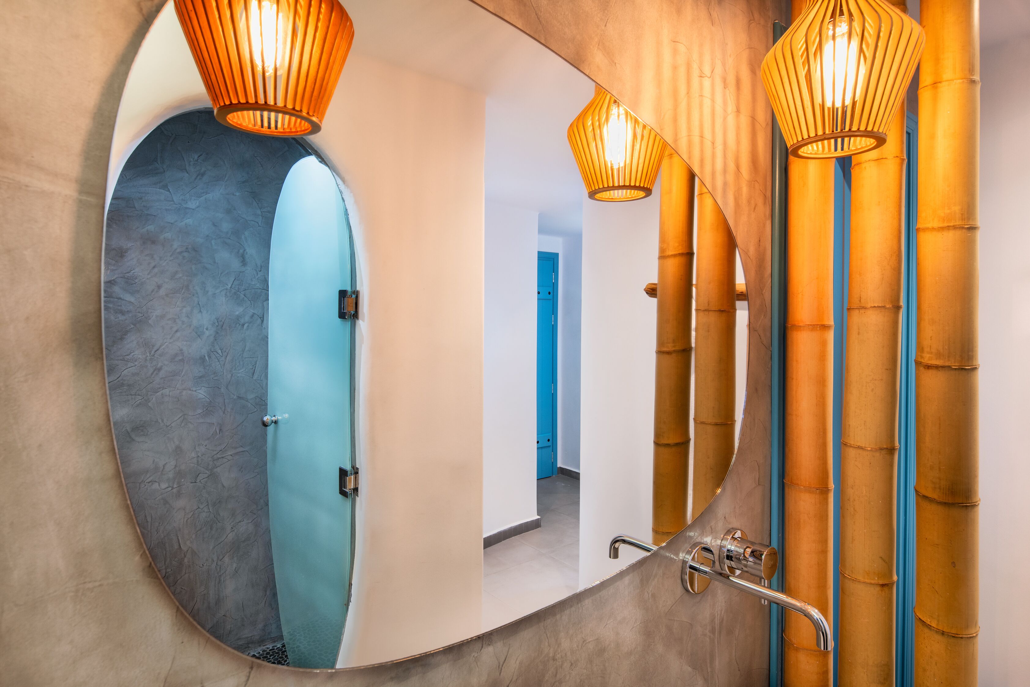 Un baño con un espejo ovalado grande, una puerta azul y paneles de pared estilo bambú.