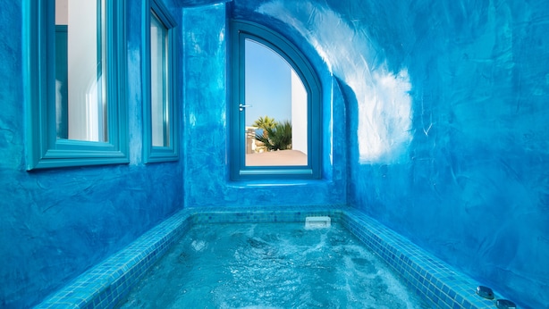 Piscina interior con azulejos azules y vistas a palmeras y edificios.