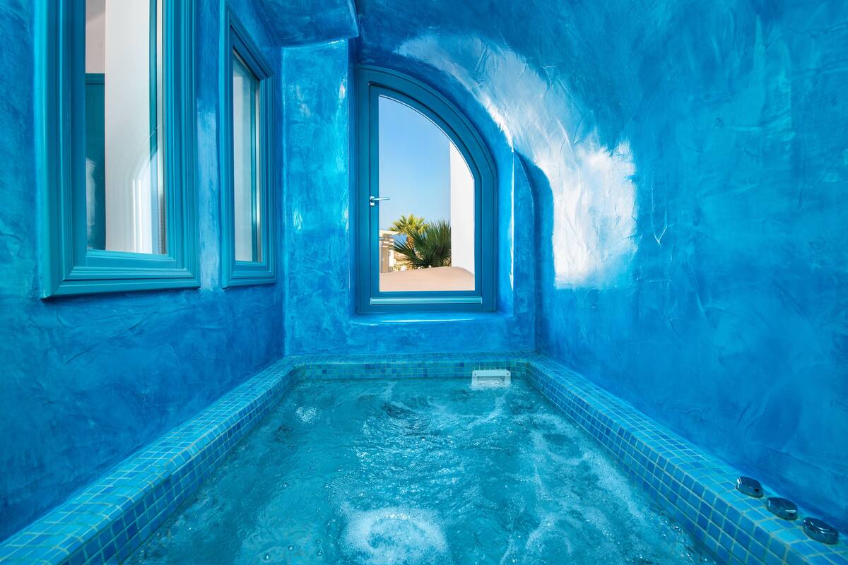 Piscina interior con azulejos azules y vistas a palmeras y edificios.