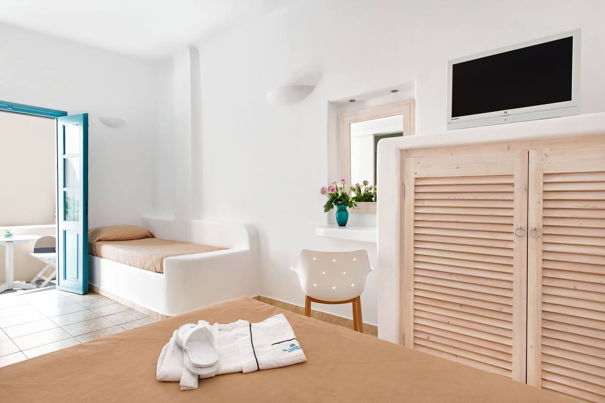 Una habitación de hotel moderna con una cama, una mesita, una silla, un televisor y un armario de madera.