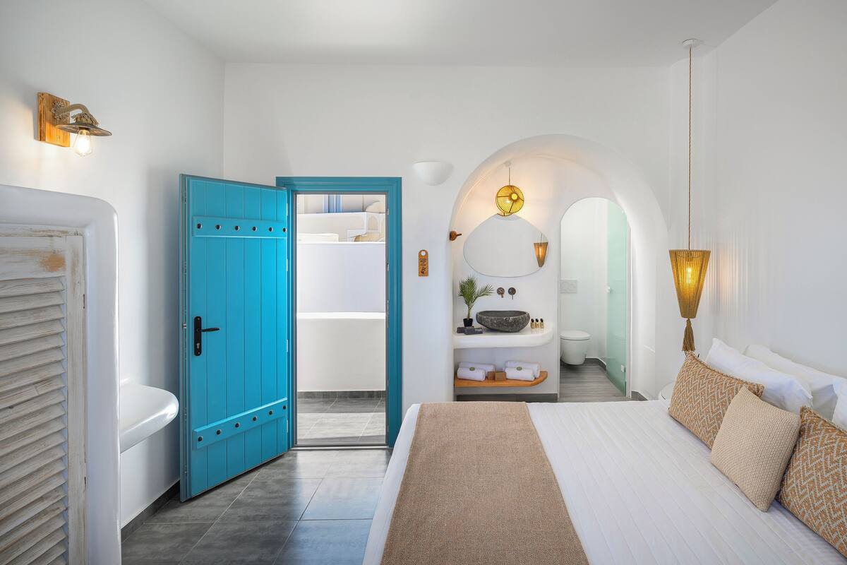 Un dormitorio con cama, un baño con lavamanos y espejo, y un pasillo que lleva a un armario.