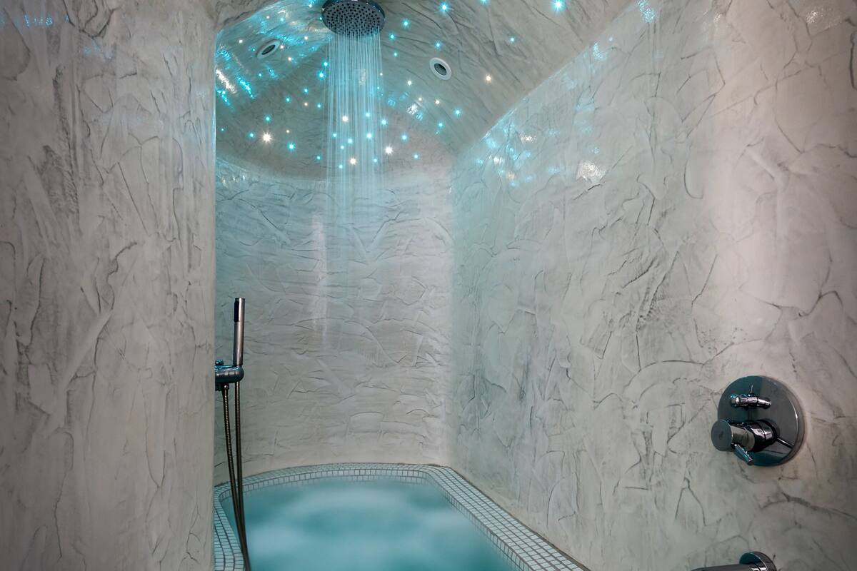 Un cuarto de spa con pared de mármol, una bañera de hidromasaje y techo con luces colgantes.