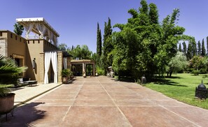 A courtyard with a tiled walkway, a covered seating area, and a variety of trees and plants.