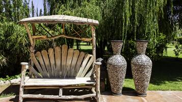 A wooden chair with a woven canopy, two intricately patterned vases, and a lush green garden in the background.