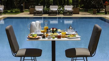 A dining table with breakfast items by a poolside, surrounded by lounge chairs.