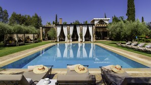 A poolside area with lounge chairs, a pool, and a building with a covered patio. - Riad Jawad & Spa (Marrakech)