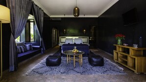 A modern bedroom with a large bed, a sofa, a coffee table, and a TV on the wall. - Riad Jawad & Spa (Marrakech)