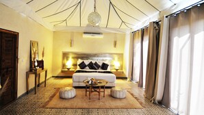 A spacious bedroom with a large bed, a round coffee table, and a hanging light fixture. - Riad Jawad & Spa (Marrakech)