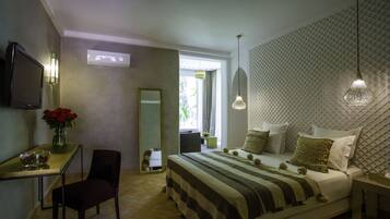 A bedroom with a bed, bedside table, chair, TV, and a desk with a vase of flowers.