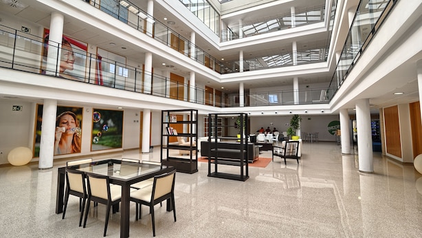 A multi-level atrium with glass railings, a central seating area, and a high ceiling with skylights.