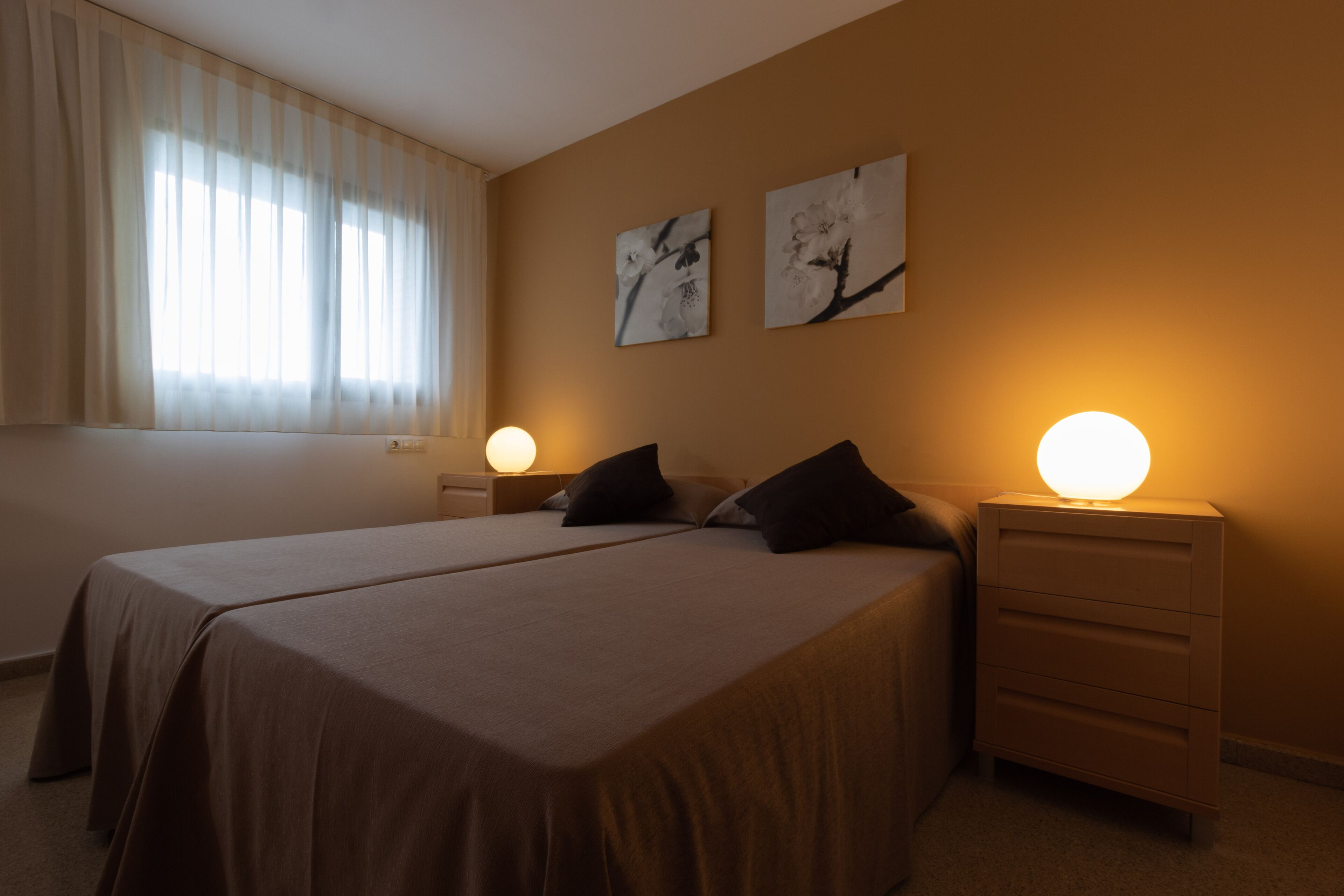 A bedroom with two beds, a nightstand with a lamp, and artwork on the wall.