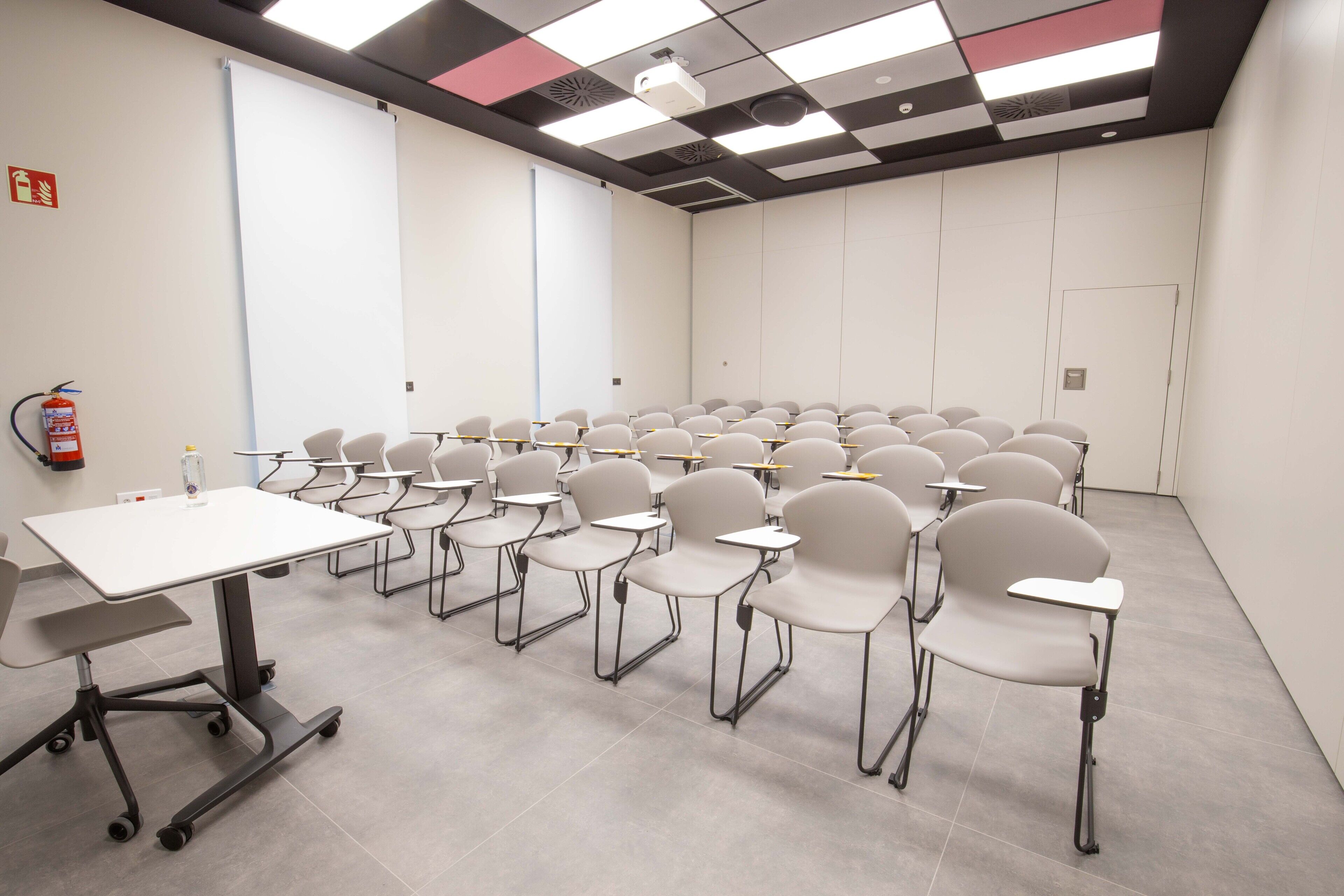 Uma sala de conferências com fileiras de cadeiras, um quadro branco e um projetor.