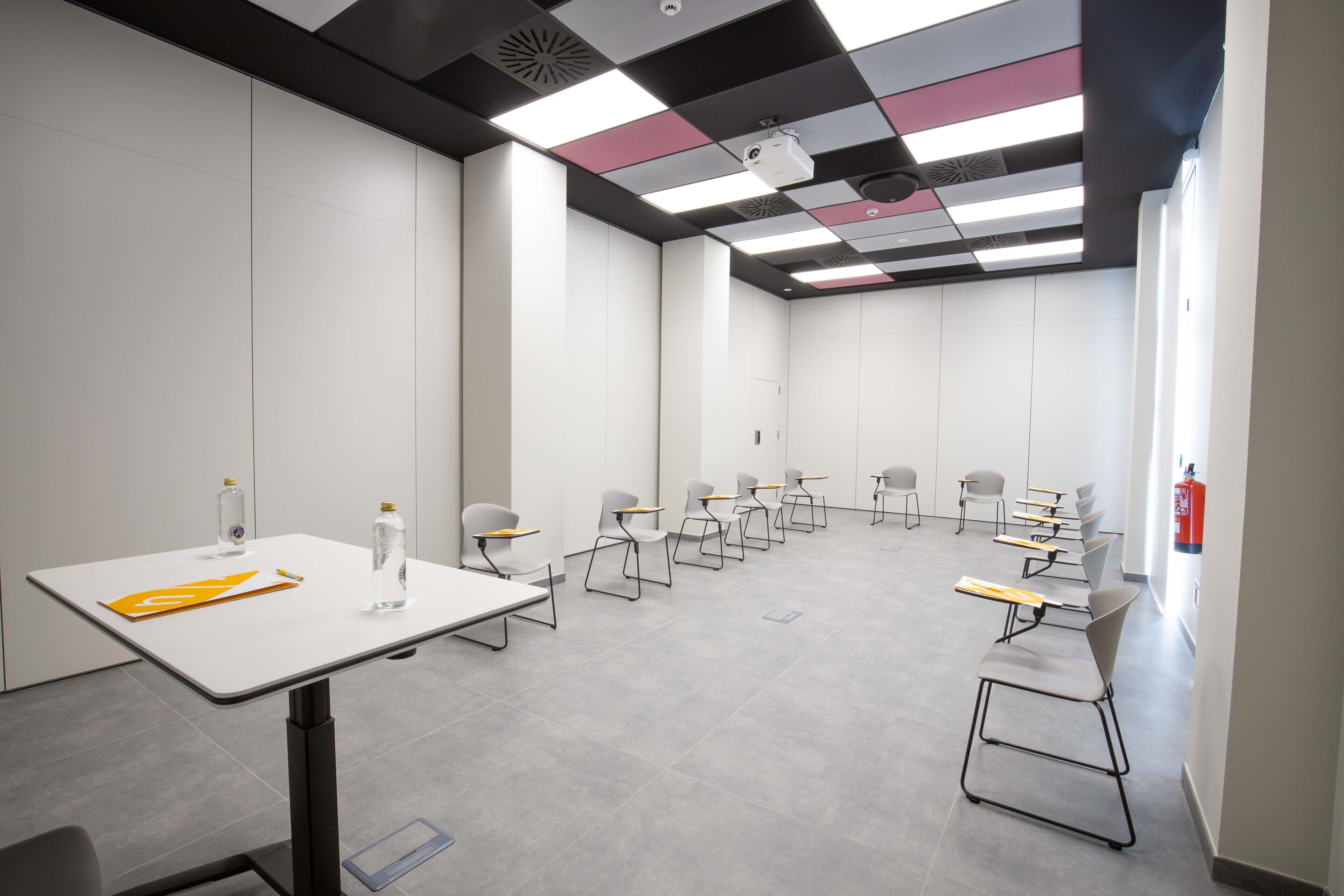 Une salle de conférence avec une table blanche, des chaises et un projecteur.