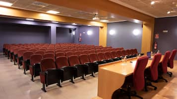 Un salón de conferencias con filas de sillas, una mesa larga y una pantalla para proyector.