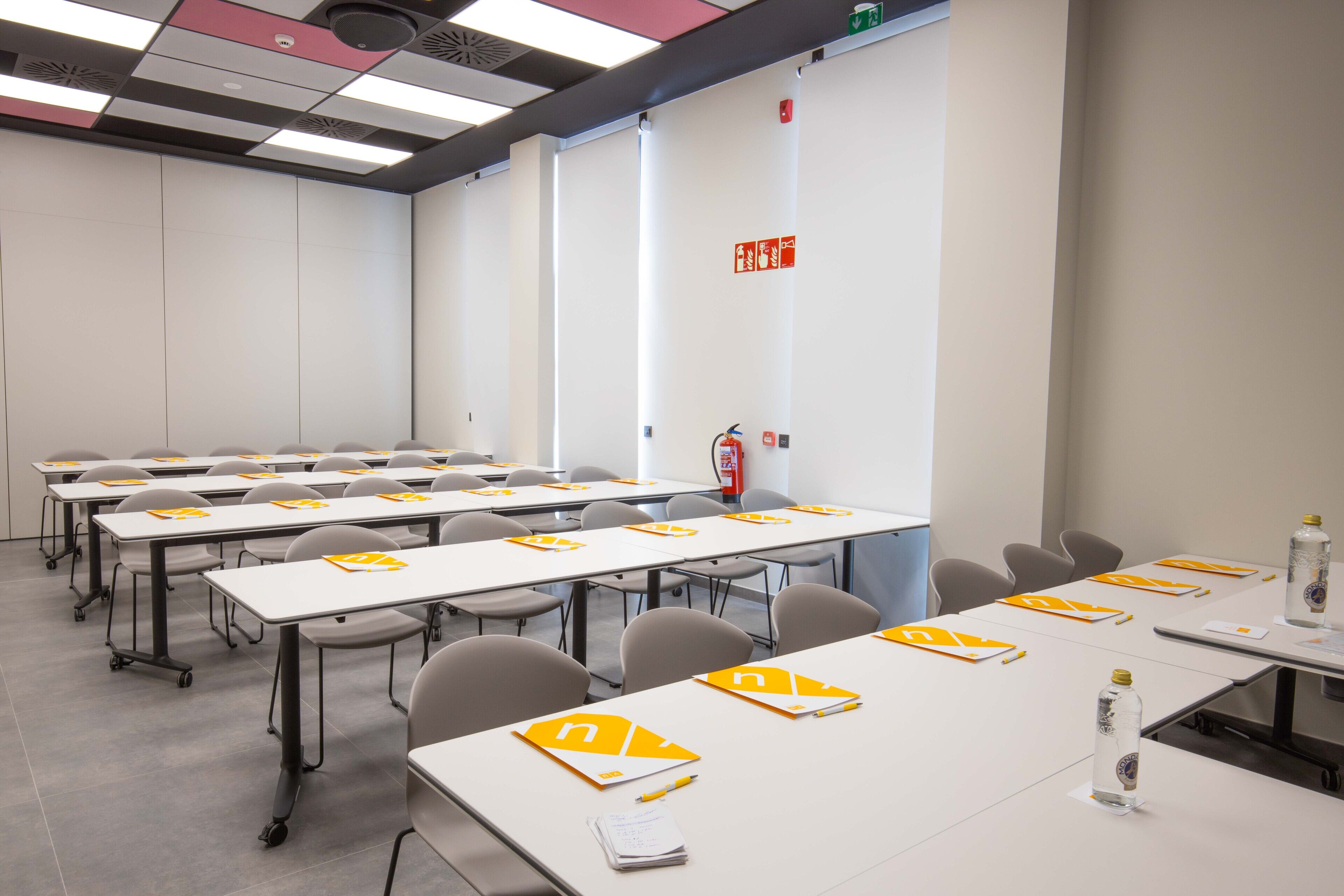 Un salón de conferencias con mesas blancas, sillas grises y carteles amarillos.
