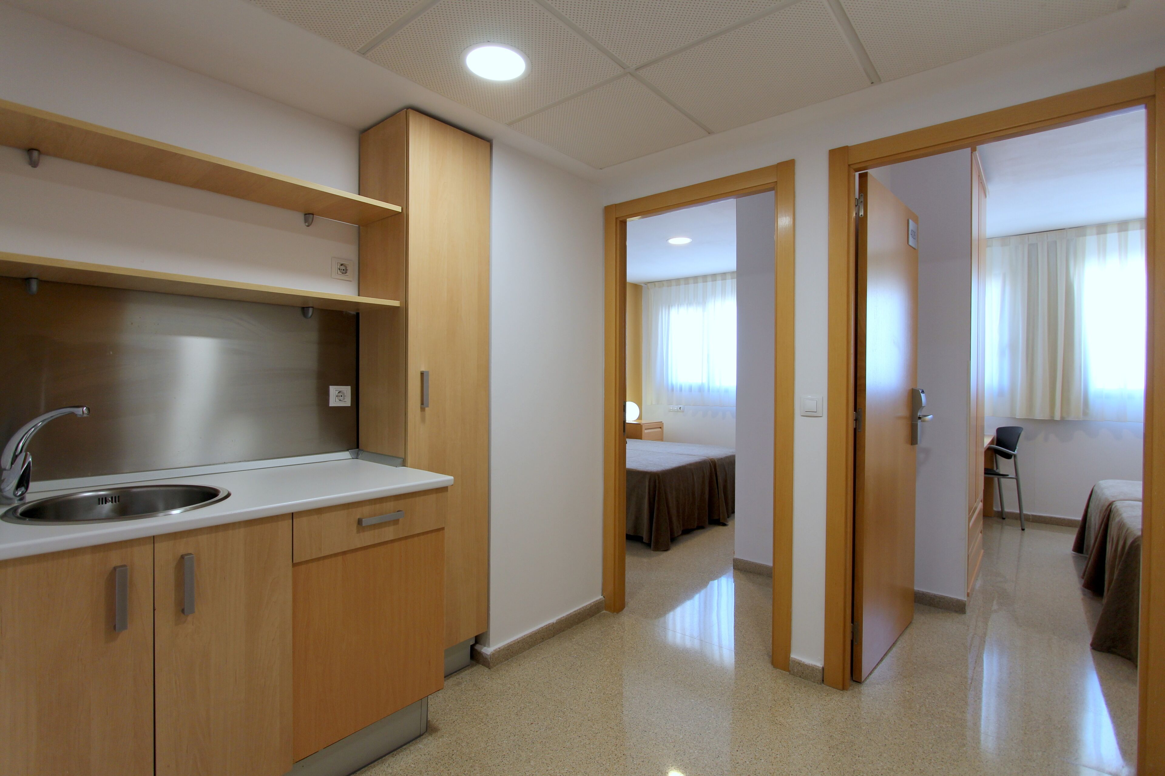 Habitación de hotel con kitchenette, una cama, una silla y una puerta que da a otra habitación.