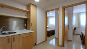 Habitación de hotel con kitchenette, una cama, una silla y una puerta que da a otra habitación.