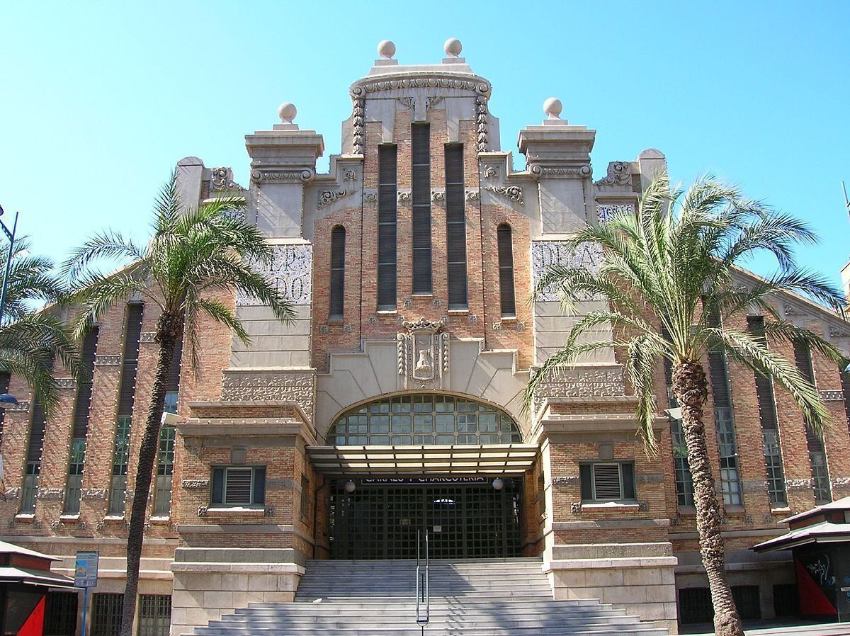 Un edificio histórico con una entrada imponente, que presenta un gran arco de entrada y una fachada simétrica con detalles decorativos.