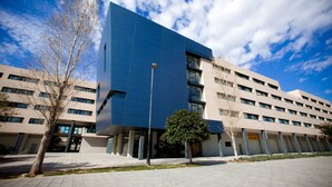 A modern building with a blue facade, multiple windows, and a clear sky.