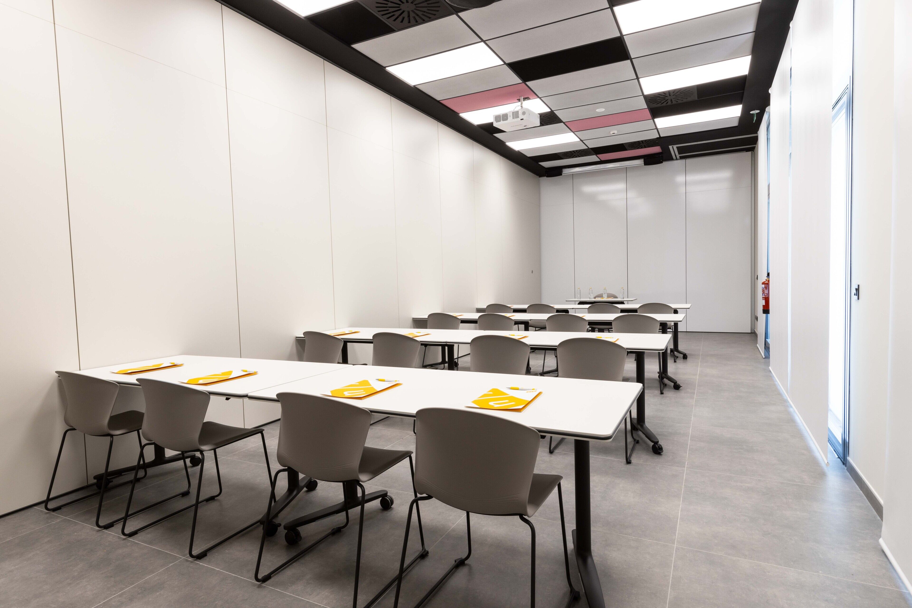 A conference room with multiple tables and chairs, a ceiling with a grid pattern, and a fire extinguisher on the wall.