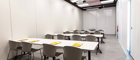 A conference room with multiple tables and chairs, a ceiling with a grid pattern, and a fire extinguisher on the wall.