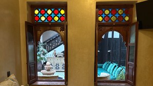 Un dormitorio con una cama, dos ventanas con vidrieras, vistas a un patio interior y techo de madera.