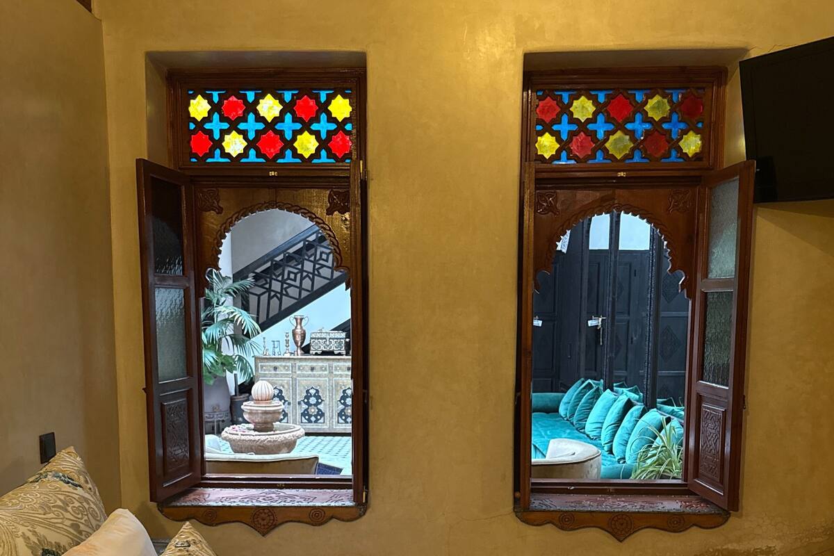 Un dormitorio con una cama, dos ventanas con vidrieras, vistas a un patio interior y techo de madera.