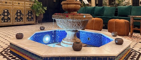 A fountain with a tiled pool in a lobby area, surrounded by a patterned floor and a sofa.
