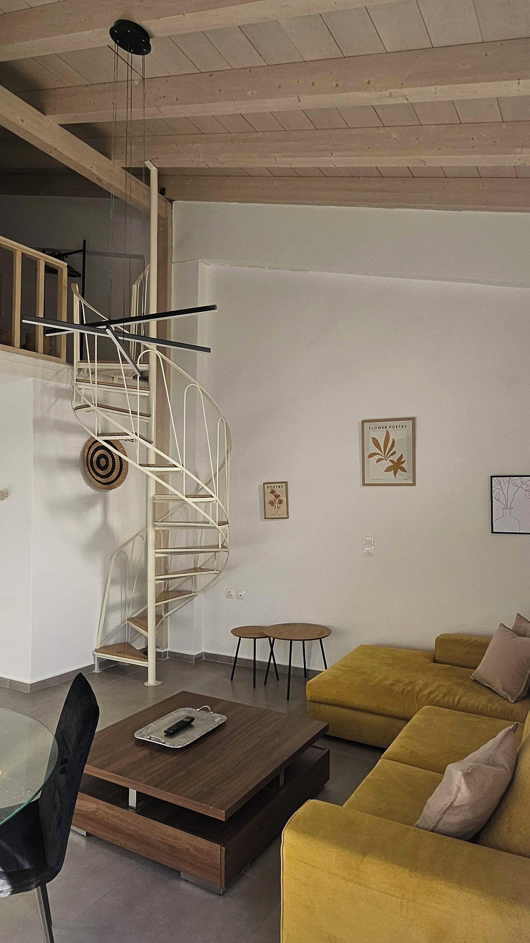 A modern living room with a yellow sofa, a wooden coffee table, a spiral staircase, and minimalist decor.