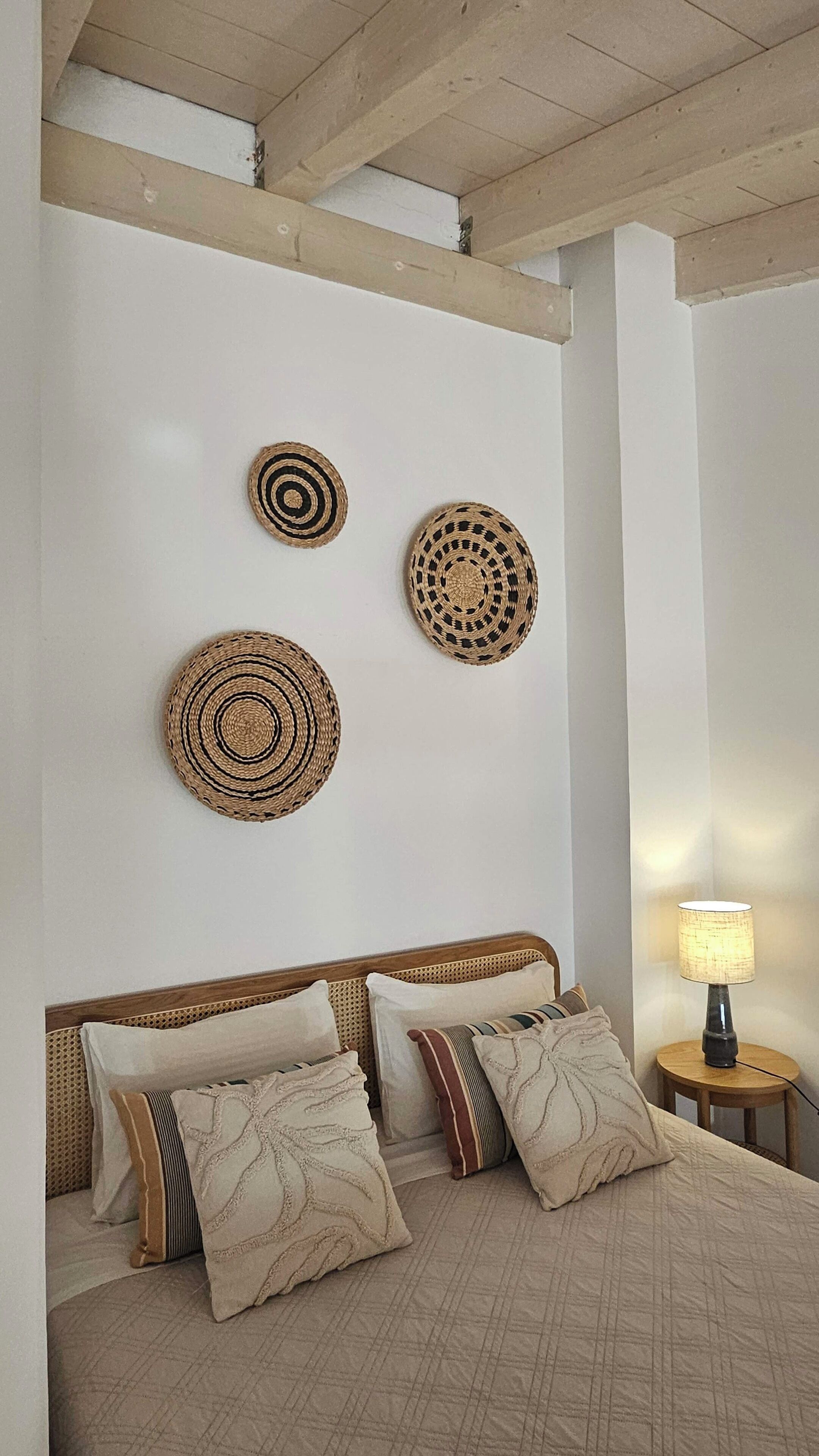 A bedroom with a wooden headboard, a bed with multiple pillows, and three woven wall hangings.