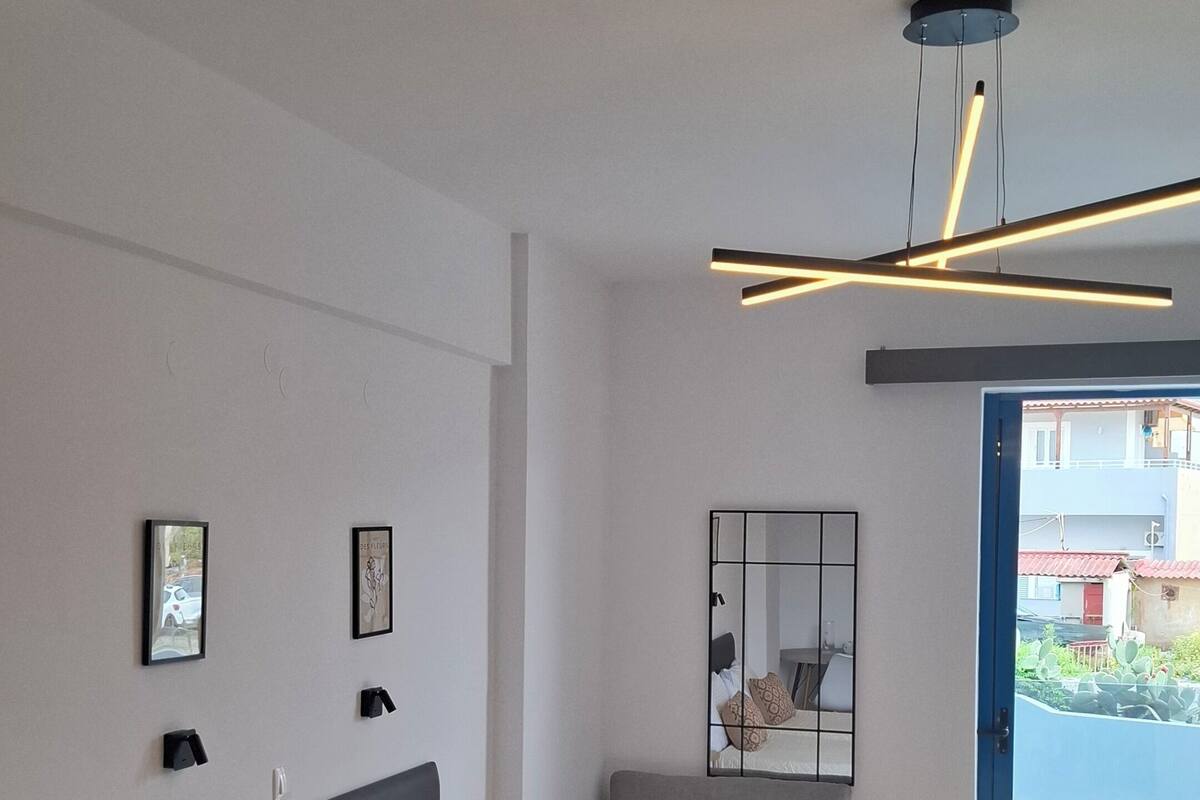 A modern hotel room with a large bed, a sofa, a small table, and a ceiling light fixture.