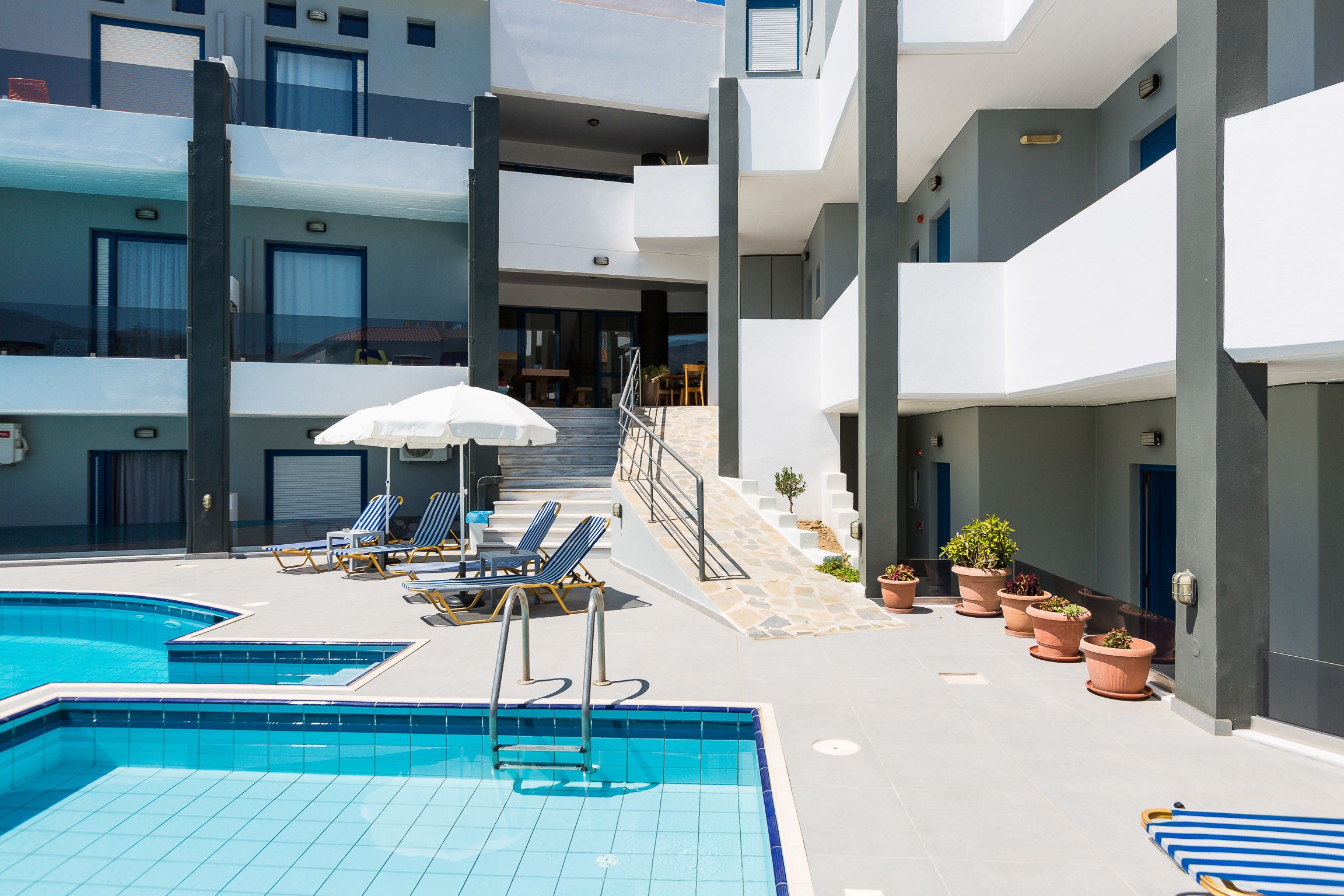 A modern hotel with a swimming pool, sun loungers, and potted plants.