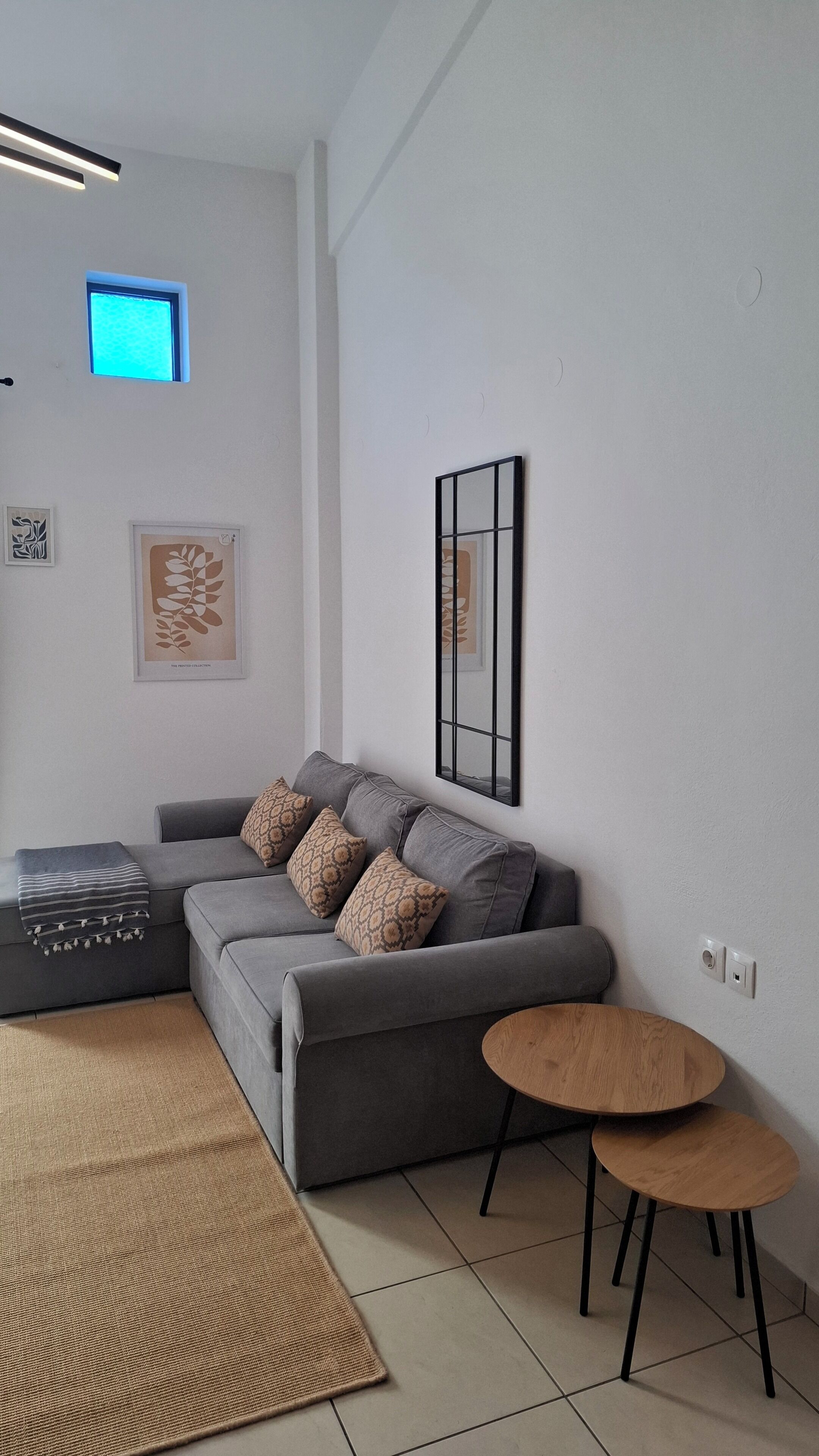 Ein modernes Wohnzimmer mit grauem Sofa, gemusterten Kissen, einem kleinen Holztisch, einem Webteppich und Wandbildern.
