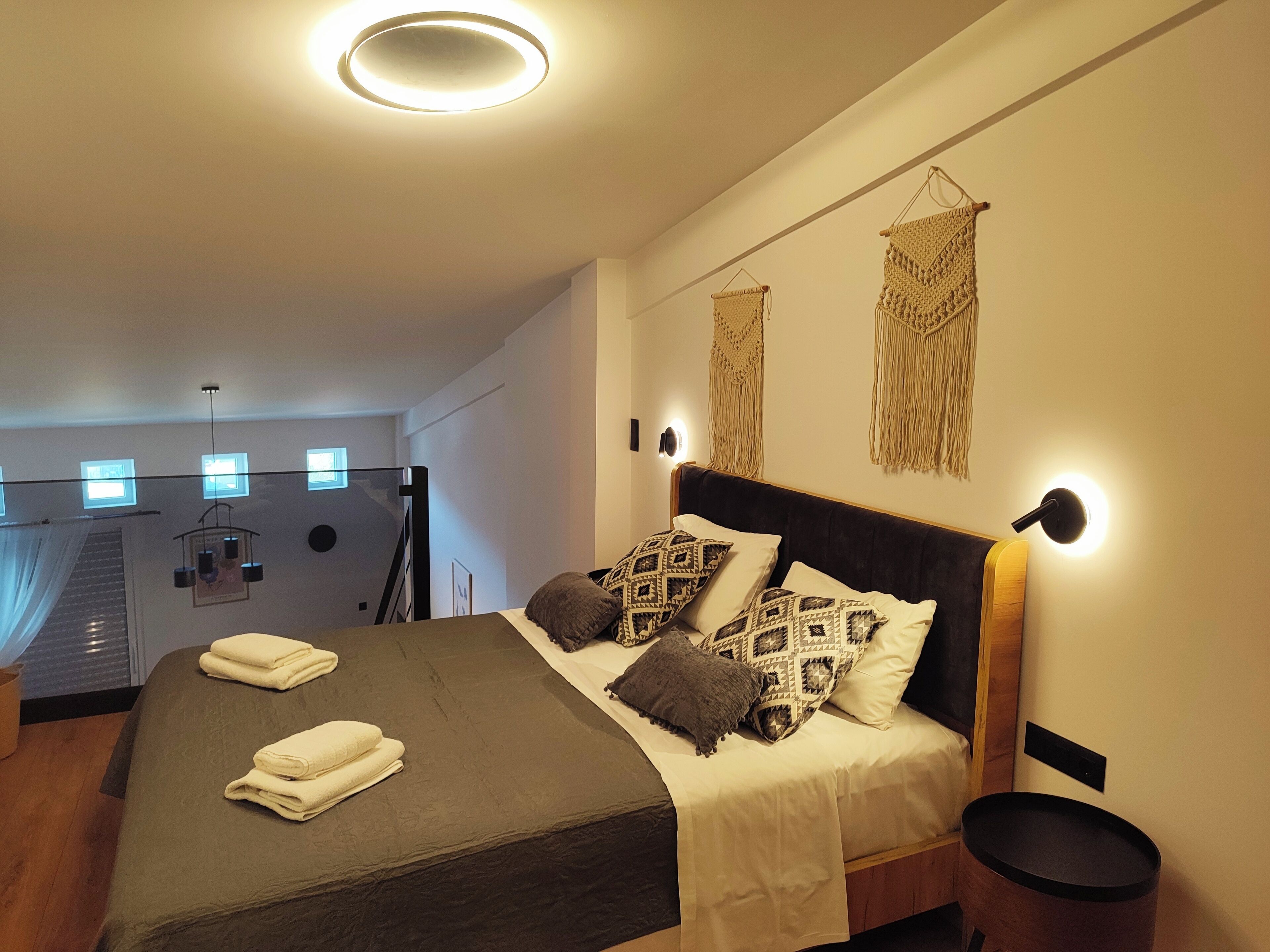 A modern bedroom with a large bed, bedside lamps, and macrame wall hangings.