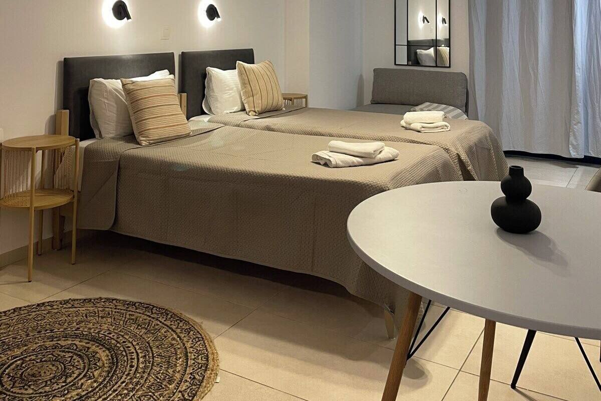 A modern hotel room with a bed, bedside tables, a round table, a rug, and a ceiling light fixture.