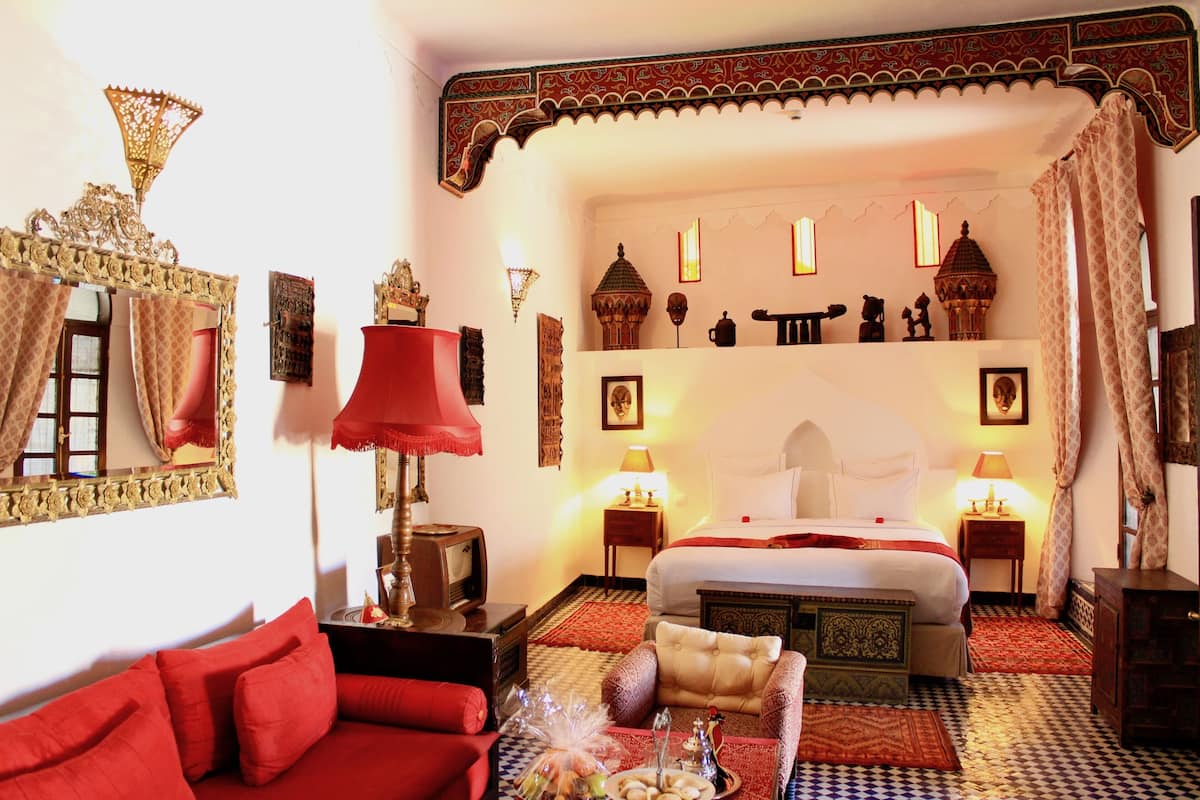A traditional Moroccan room with a large bed, red furniture, and ornate decor.