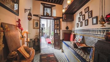 Un pasillo estrecho con baldosas estampadas, un banco de madera y un vano que da a otra habitación.