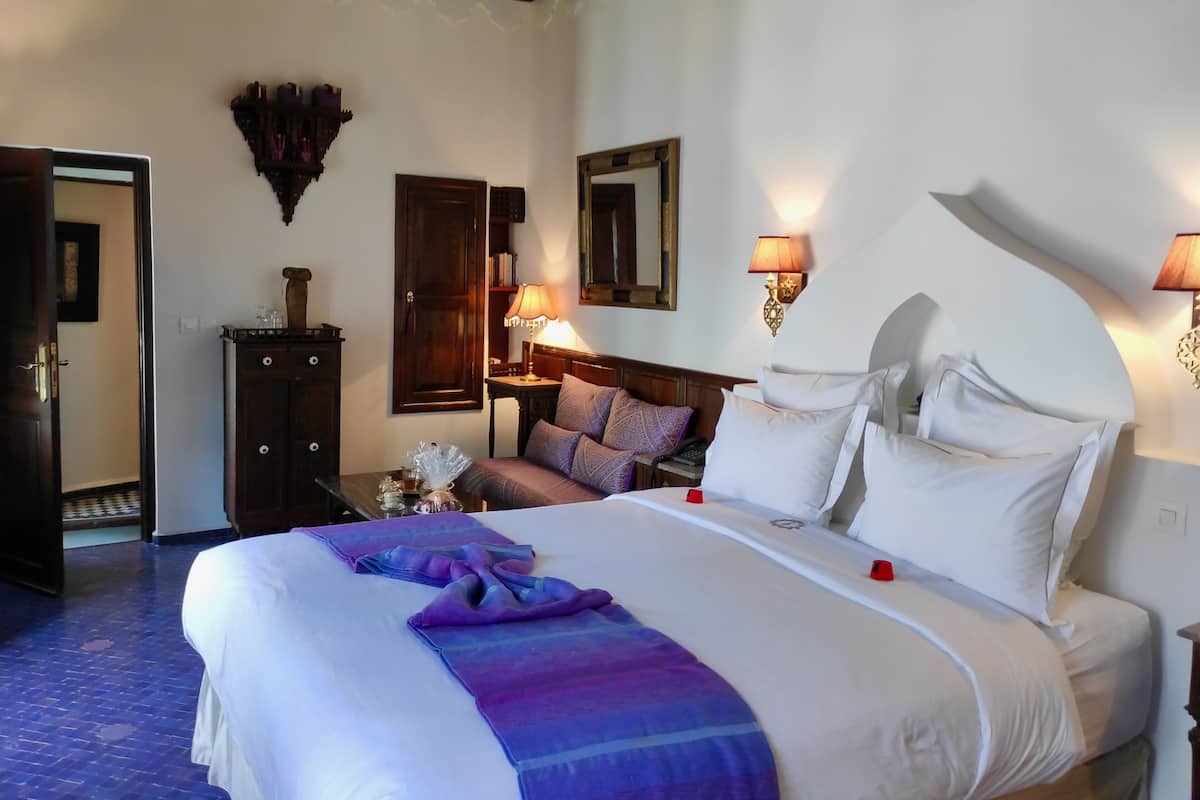 A hotel room with a large bed, bedside lamps, a wooden headboard, a nightstand, and a mirror on the wall.