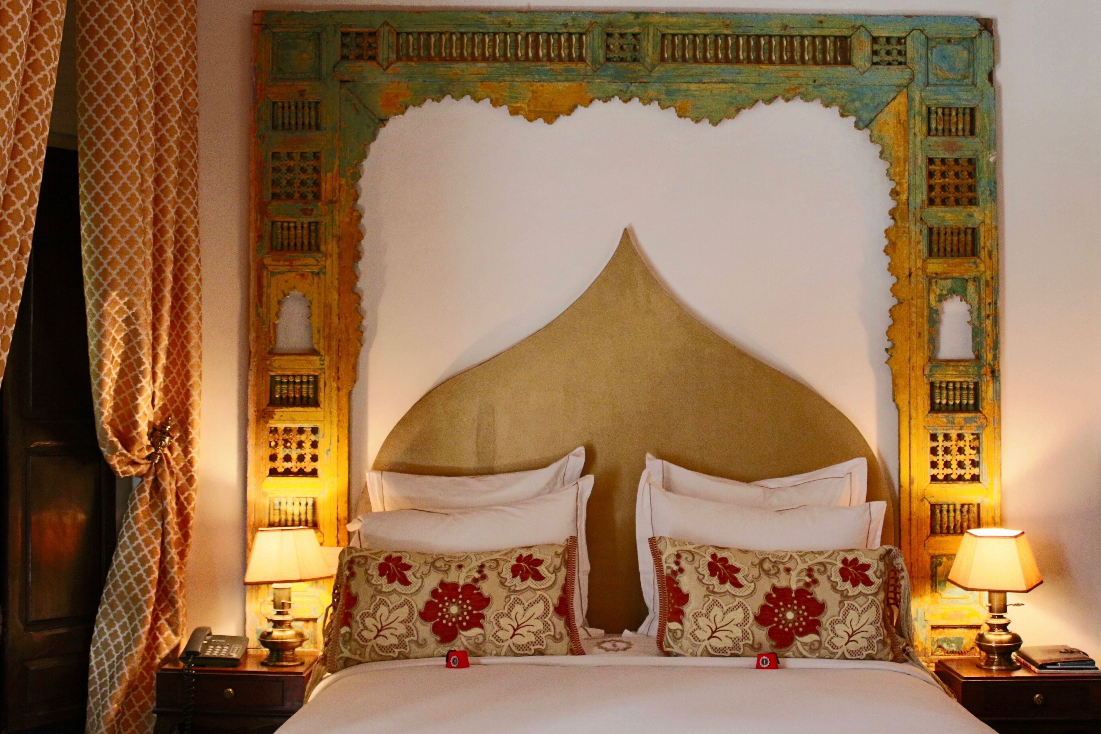 A bed with a decorative headboard, two bedside tables with lamps, and a patterned curtain.
