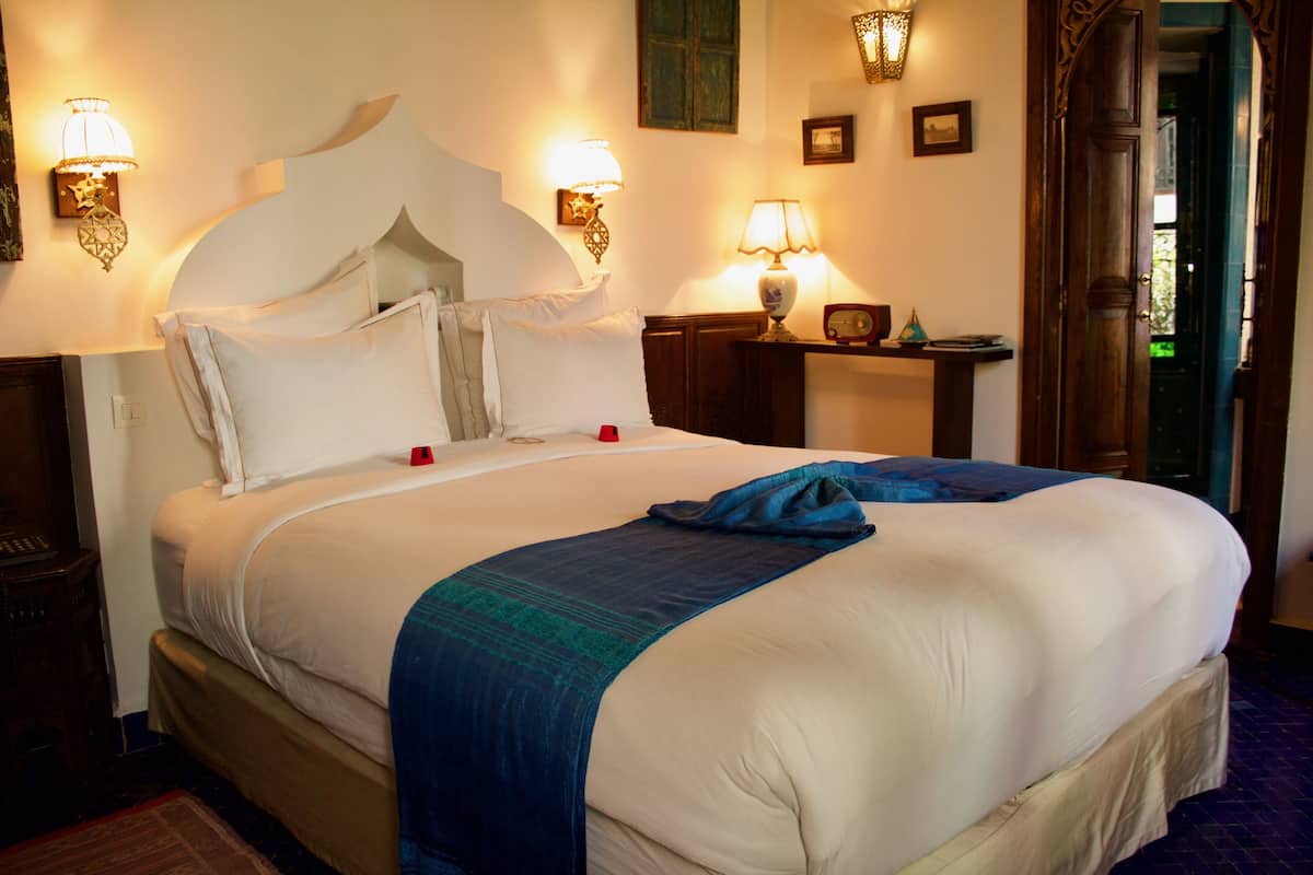 A neatly made bed with a white headboard, two bedside lamps, and a nightstand with a radio.