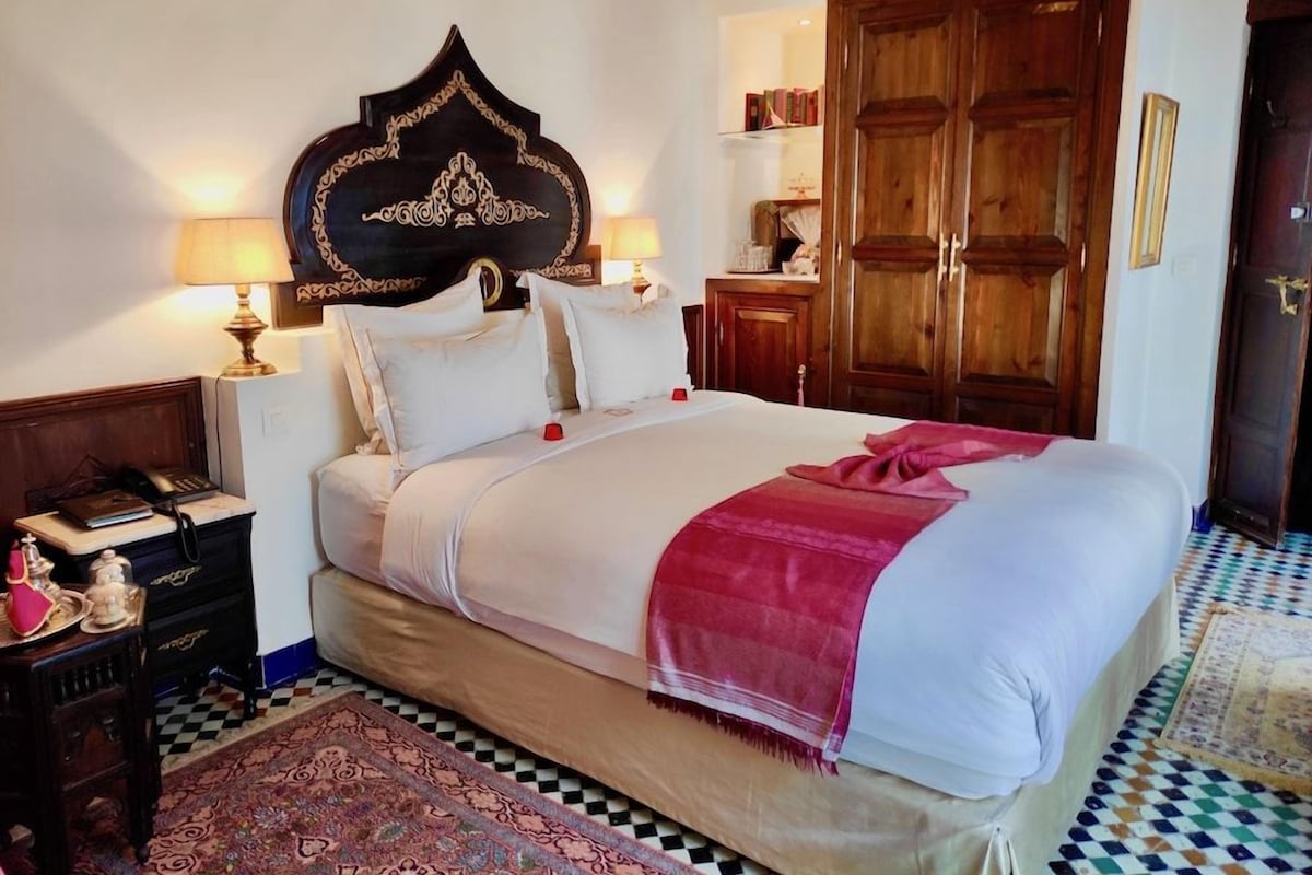 A neatly made bed with a headboard, bedside tables with lamps, a large wooden wardrobe, and a patterned rug.