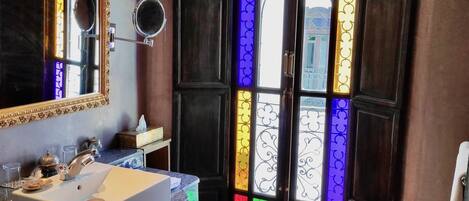 A bathroom with a large mirror, a sink, and a decorative door with stained glass.