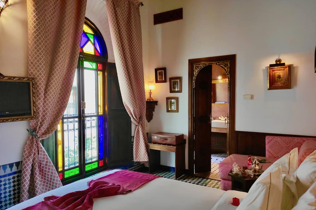 A hotel room with a bed, a bedside table, a mirror, and a window with curtains.