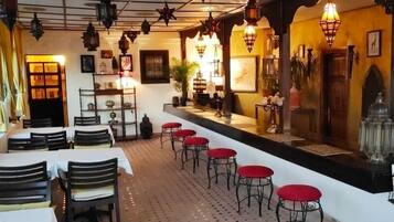 Un restaurant avec des tables et des tabourets rouges, un coin bar avec un comptoir et un éclairage décoratif.