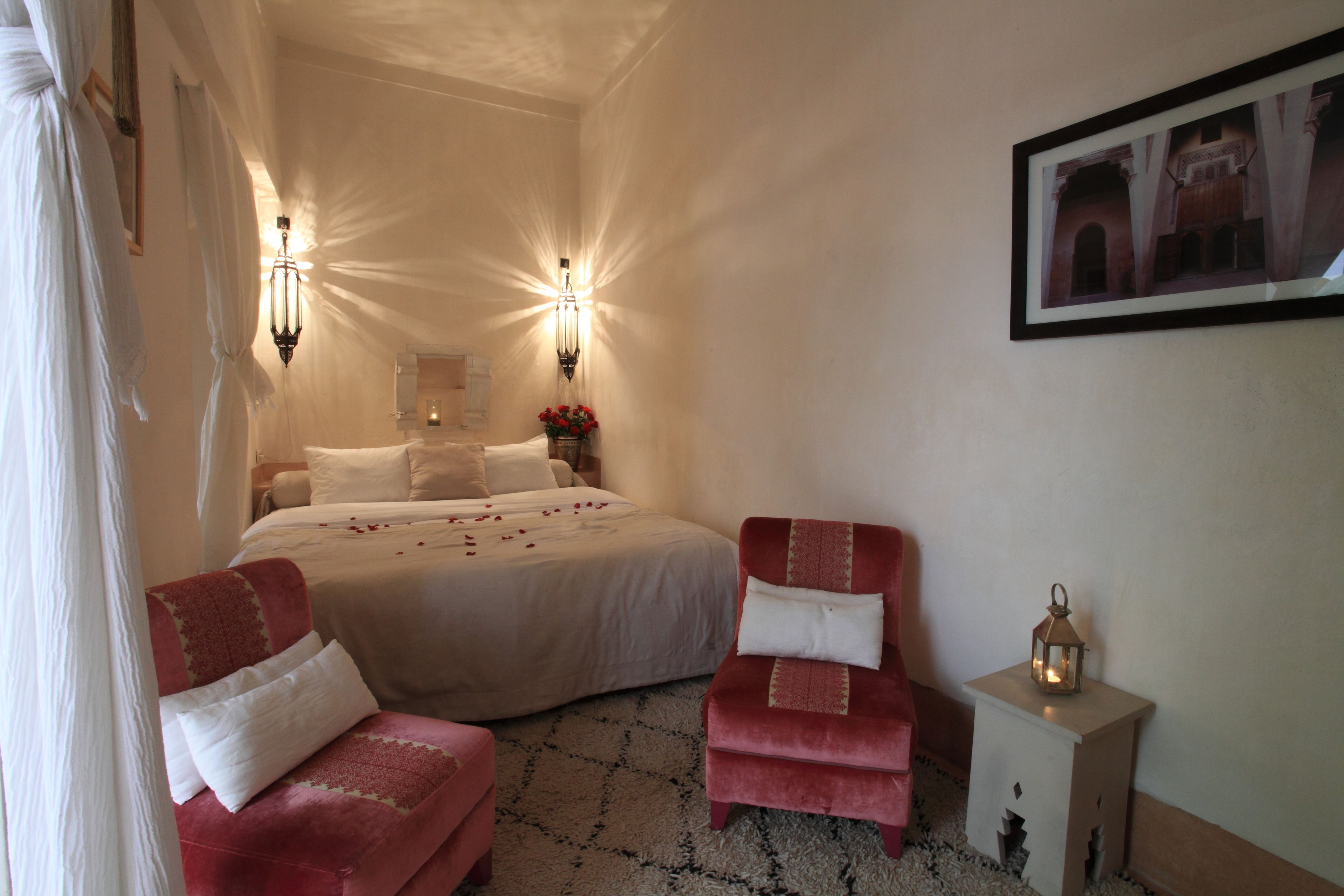 Quarto com cama grande, duas cadeiras, mesa de cabeceira com lanterna e quadro pendurado na parede.