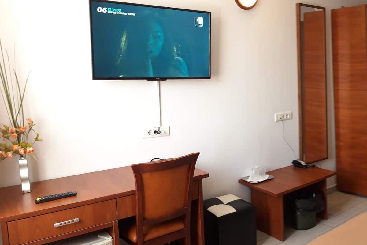 Una camera d'albergo con un letto, una scrivania con una sedia, una TV a parete e un grande murale con vista sulla città.