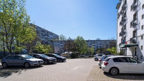 En parkeringsplats med flera bilar, en byggnad med flera våningar och balkonger samt träd med gröna löv.